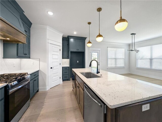 kitchen with sink, appliances with stainless steel finishes, a kitchen island with sink, light stone countertops, and decorative light fixtures