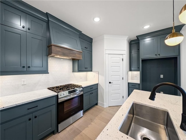 kitchen with stainless steel gas range, sink, light stone counters, hanging light fixtures, and light hardwood / wood-style flooring