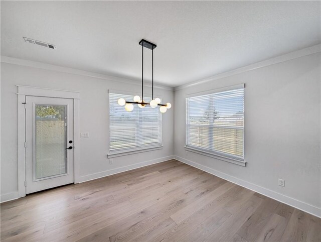 unfurnished dining area with crown molding, light wood-type flooring, and a notable chandelier