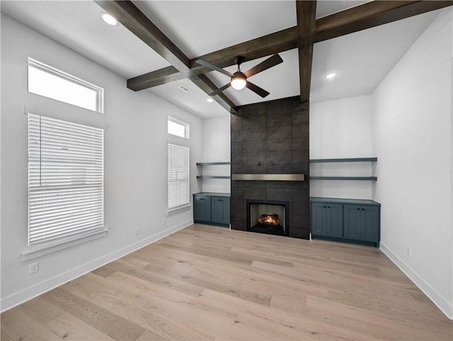 unfurnished living room featuring ceiling fan, a large fireplace, beam ceiling, and light hardwood / wood-style flooring