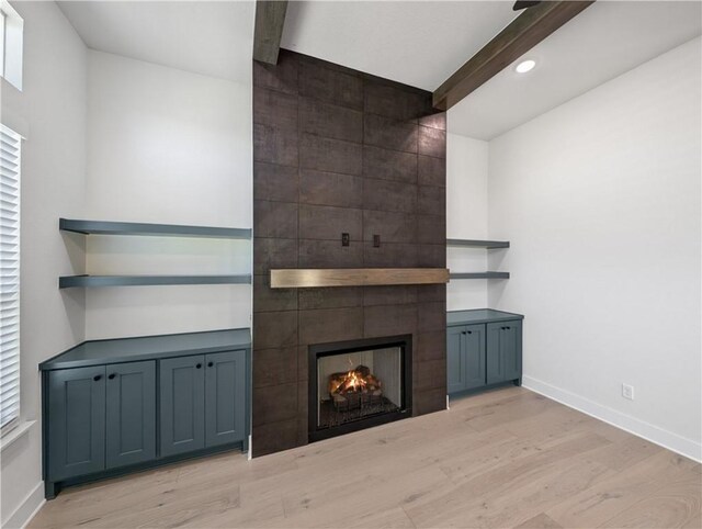 unfurnished living room featuring light hardwood / wood-style flooring, beam ceiling, and a fireplace