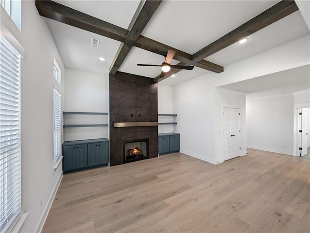 unfurnished living room featuring ceiling fan, a fireplace, light hardwood / wood-style floors, and beamed ceiling