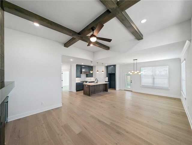 unfurnished living room with beamed ceiling, wood-type flooring, sink, and ceiling fan with notable chandelier