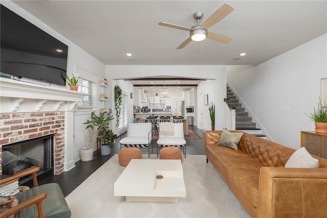 living room featuring wood-type flooring, a brick fireplace, ceiling fan, and a textured ceiling