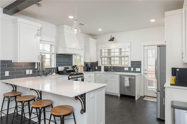 kitchen featuring premium range hood, a breakfast bar area, white cabinetry, appliances with stainless steel finishes, and pendant lighting