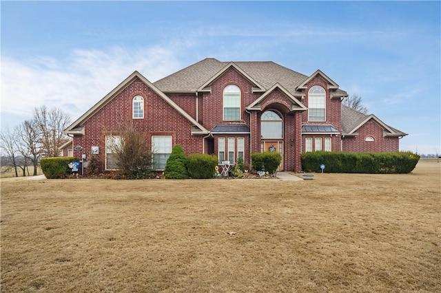 traditional-style home with a front lawn, brick siding, and a shingled roof