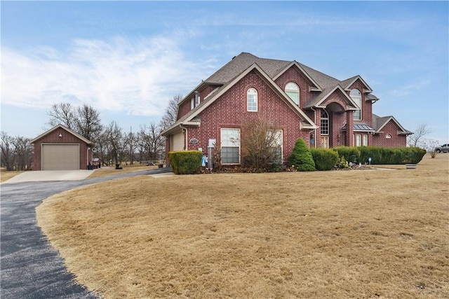 view of front facade featuring brick siding, an outdoor structure, a detached garage, and a front yard