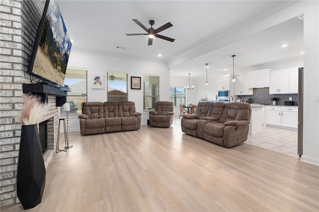 living room with crown molding, a fireplace, ceiling fan, and light wood-type flooring