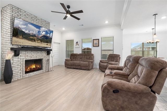 living room with ornamental molding, a brick fireplace, ceiling fan with notable chandelier, and light hardwood / wood-style flooring