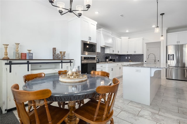 kitchen featuring appliances with stainless steel finishes, a kitchen island with sink, white cabinetry, light stone countertops, and custom range hood