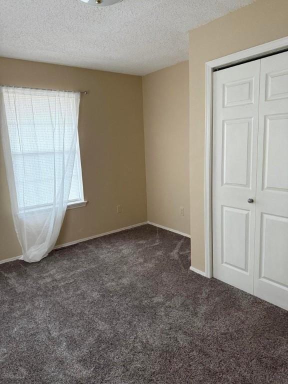 unfurnished bedroom with a closet, dark carpet, and a textured ceiling