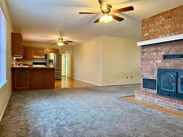 unfurnished living room featuring light carpet, a brick fireplace, and ceiling fan