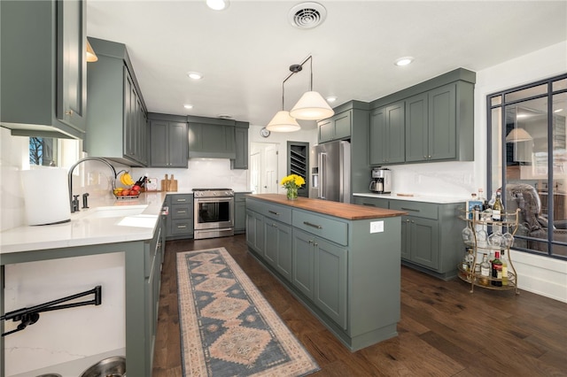 kitchen featuring butcher block countertops, decorative light fixtures, sink, backsplash, and stainless steel appliances