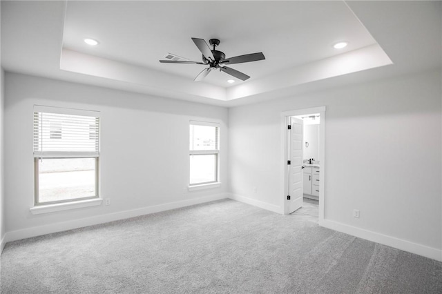 carpeted spare room with a raised ceiling and ceiling fan