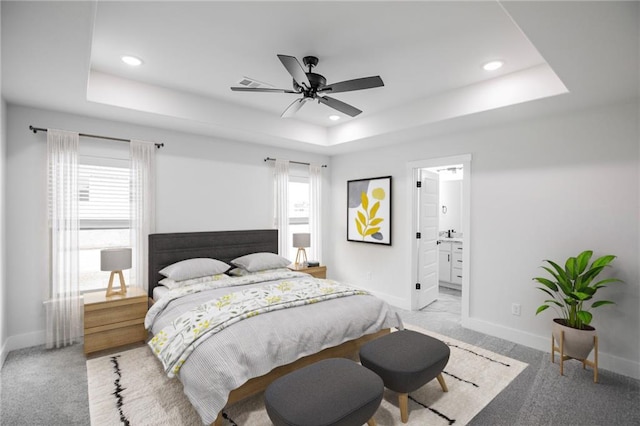 carpeted bedroom with multiple windows, ensuite bath, ceiling fan, and a tray ceiling