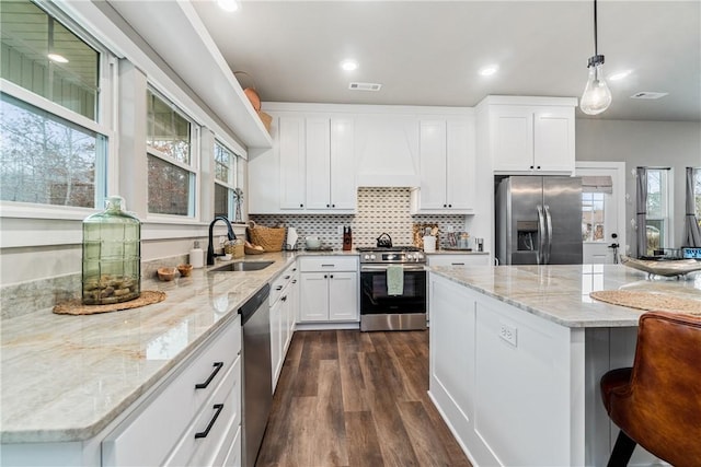 kitchen featuring sink, premium range hood, stainless steel appliances, white cabinets, and decorative light fixtures