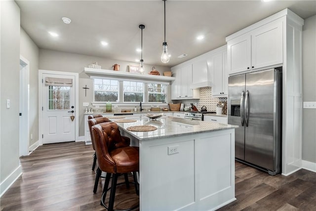 kitchen featuring white cabinets, a center island, light stone counters, stainless steel appliances, and custom range hood