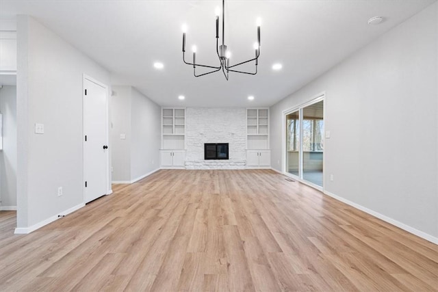 unfurnished living room featuring an inviting chandelier, a fireplace, built in features, and light wood-type flooring