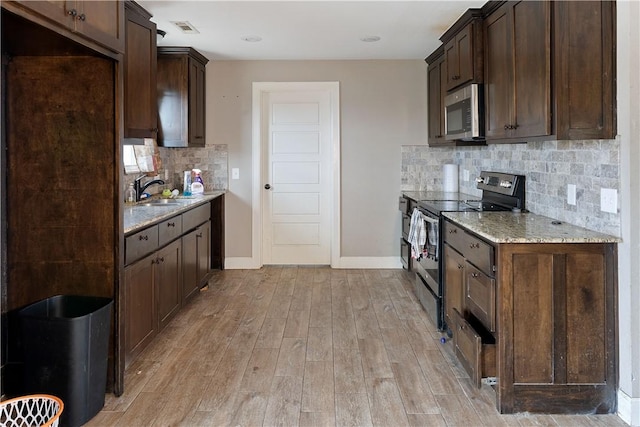 kitchen with dark brown cabinetry, sink, light stone counters, light wood-type flooring, and stainless steel appliances