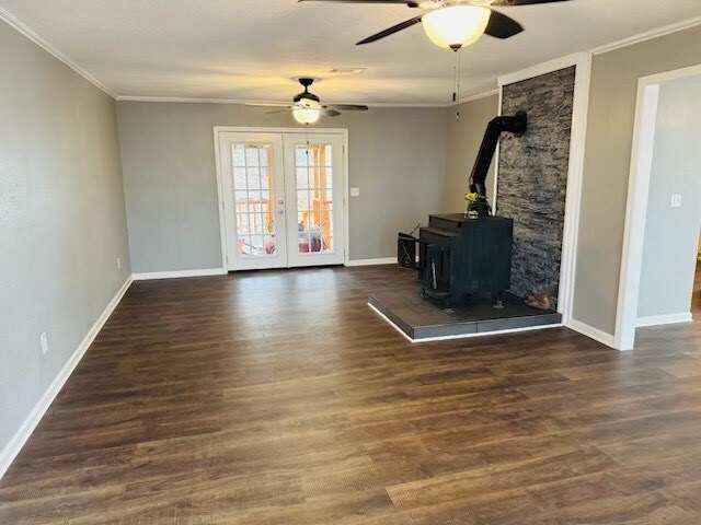 unfurnished living room featuring dark hardwood / wood-style floors, ornamental molding, french doors, and a wood stove