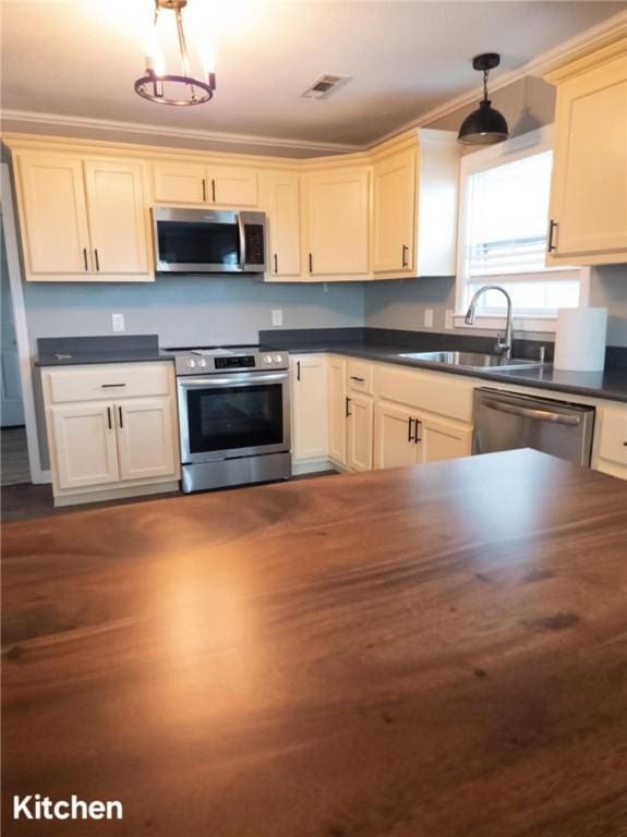 kitchen with dark countertops, appliances with stainless steel finishes, hanging light fixtures, crown molding, and a sink