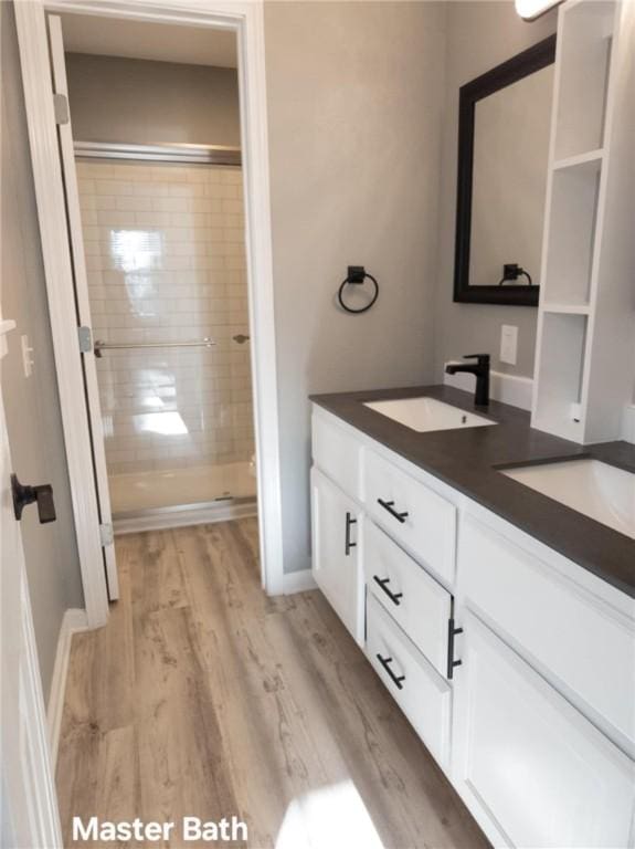 bathroom with wood finished floors, a sink, a tile shower, and double vanity