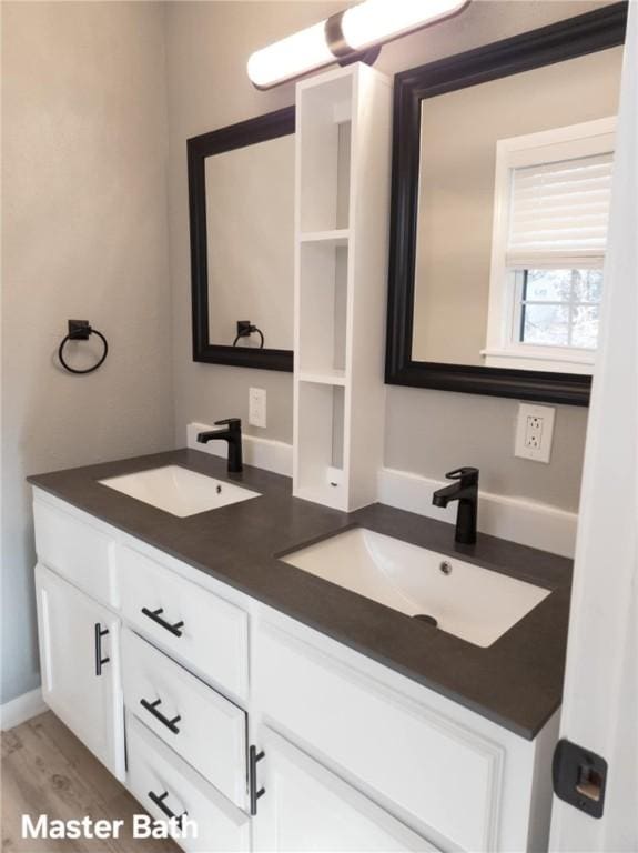 full bathroom with double vanity, wood finished floors, a sink, and baseboards