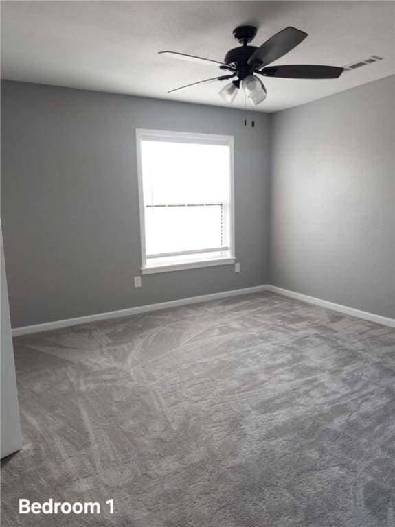 carpeted empty room with baseboards, visible vents, and a ceiling fan