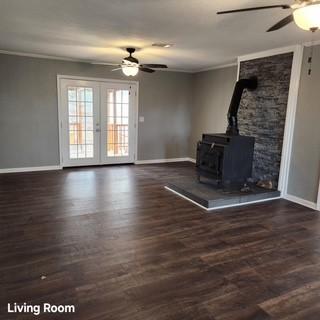 unfurnished living room with french doors, dark wood-style flooring, ornamental molding, a ceiling fan, and a wood stove