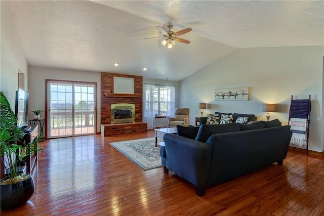 living room featuring dark hardwood / wood-style floors, lofted ceiling, ceiling fan, a brick fireplace, and a textured ceiling