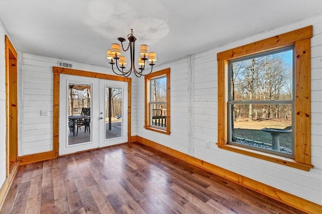 empty room featuring an inviting chandelier, dark hardwood / wood-style flooring, french doors, and wood walls