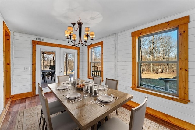 dining room with an inviting chandelier, hardwood / wood-style flooring, french doors, and wood walls