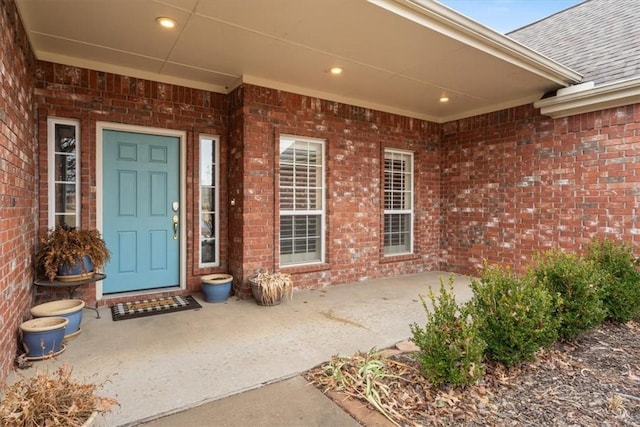 view of exterior entry featuring a shingled roof and brick siding