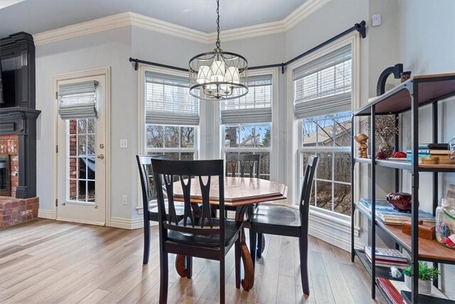 dining space featuring ornamental molding, a fireplace, a chandelier, and light wood-type flooring