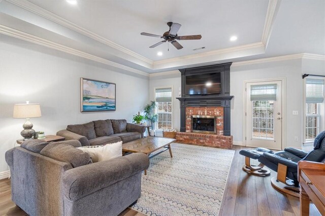 living room featuring ornamental molding, a tray ceiling, ceiling fan, a fireplace, and light hardwood / wood-style floors