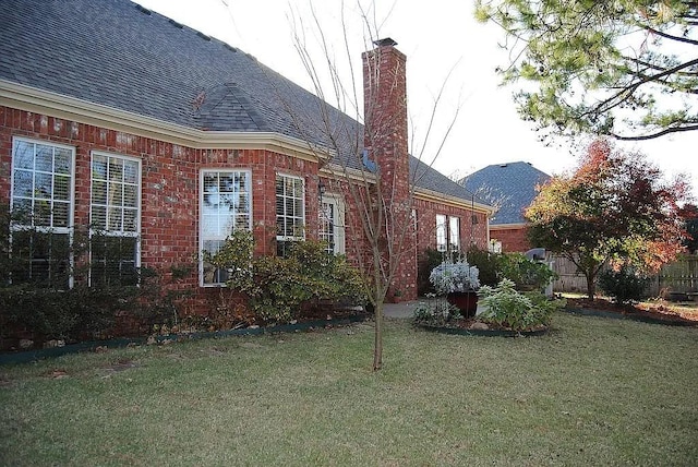 view of property exterior with a yard, brick siding, a chimney, and a shingled roof