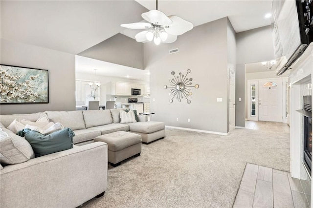 living room with high vaulted ceiling, ceiling fan with notable chandelier, and light colored carpet