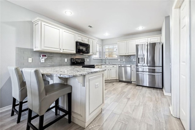 kitchen featuring a breakfast bar area, black appliances, white cabinets, decorative backsplash, and kitchen peninsula