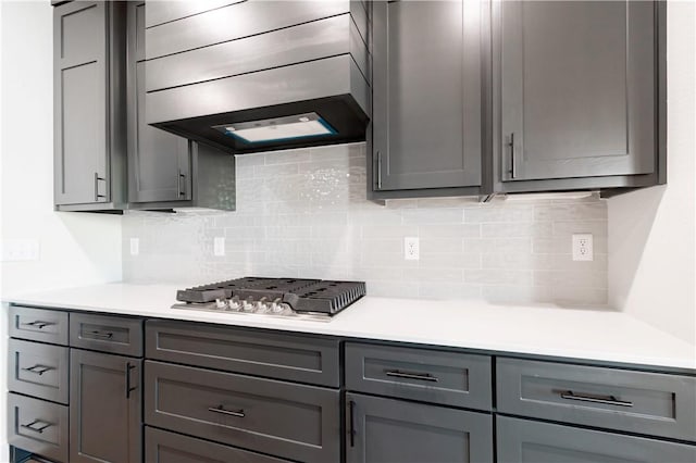 1200 Carrara St, Tontitown, AR 72762 - kitchen with gray cabinetry, premium range hood, decorative backsplash, light countertops, and stainless steel gas stovetop