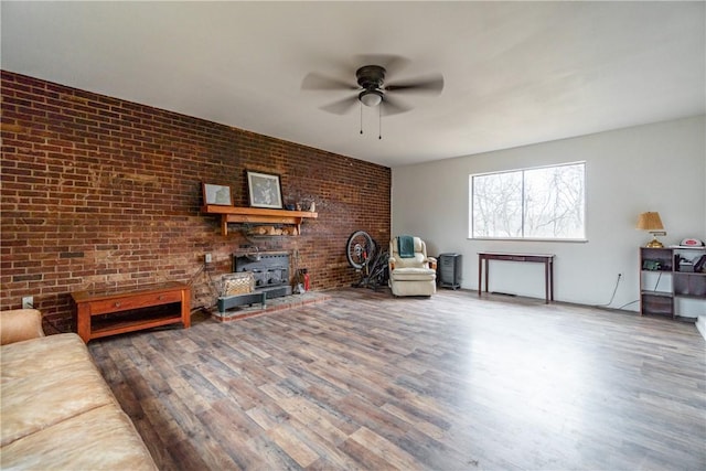 living area with brick wall, a wood stove, ceiling fan, and wood finished floors