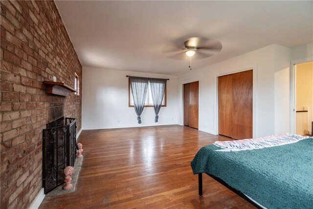 bedroom featuring baseboards, a ceiling fan, a fireplace, multiple closets, and wood finished floors