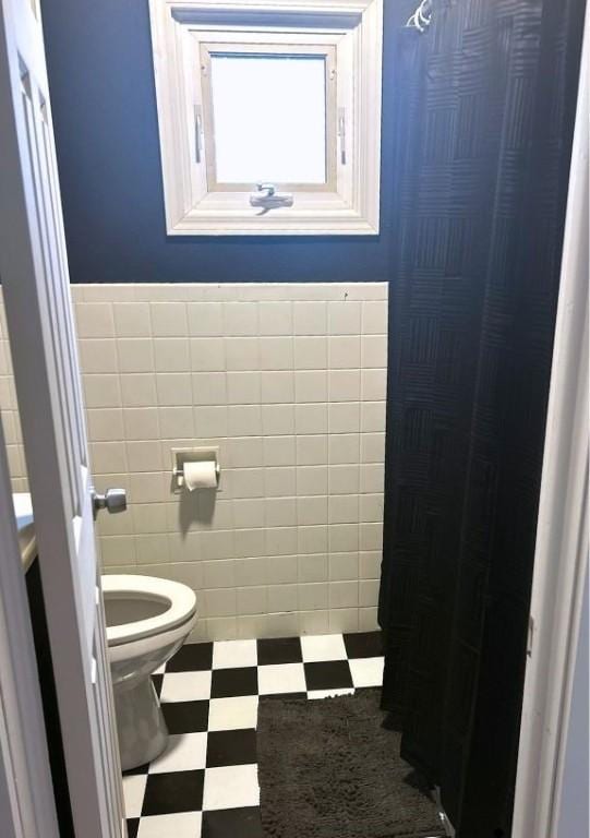 bathroom featuring toilet, tile patterned floors, wainscoting, and tile walls