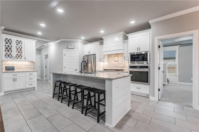 kitchen with a breakfast bar, light stone counters, a center island with sink, appliances with stainless steel finishes, and white cabinets