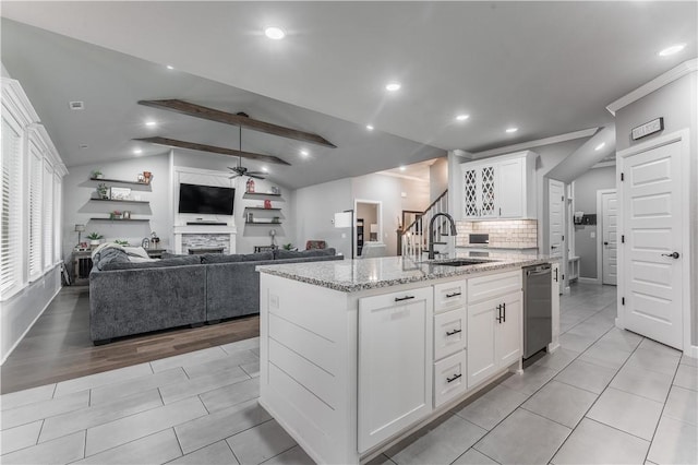 kitchen featuring sink, light stone counters, lofted ceiling with beams, white cabinets, and a center island with sink