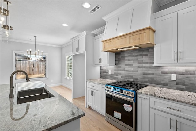 kitchen featuring pendant lighting, sink, white cabinetry, light stone counters, and stainless steel range with gas cooktop