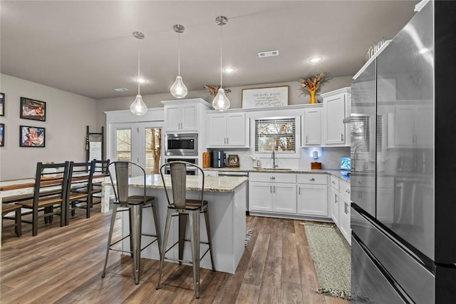 kitchen with a kitchen island, decorative light fixtures, white cabinetry, stainless steel appliances, and light stone countertops