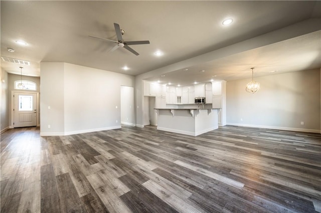 unfurnished living room with dark wood-type flooring and ceiling fan with notable chandelier