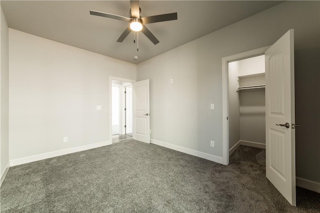 unfurnished bedroom with a spacious closet, a closet, ceiling fan, and dark colored carpet