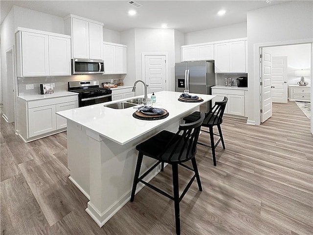 kitchen featuring sink, a kitchen breakfast bar, stainless steel appliances, a kitchen island with sink, and white cabinets