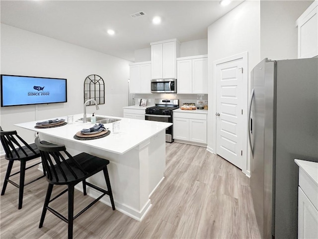 kitchen featuring sink, a kitchen island with sink, stainless steel appliances, a kitchen breakfast bar, and white cabinets